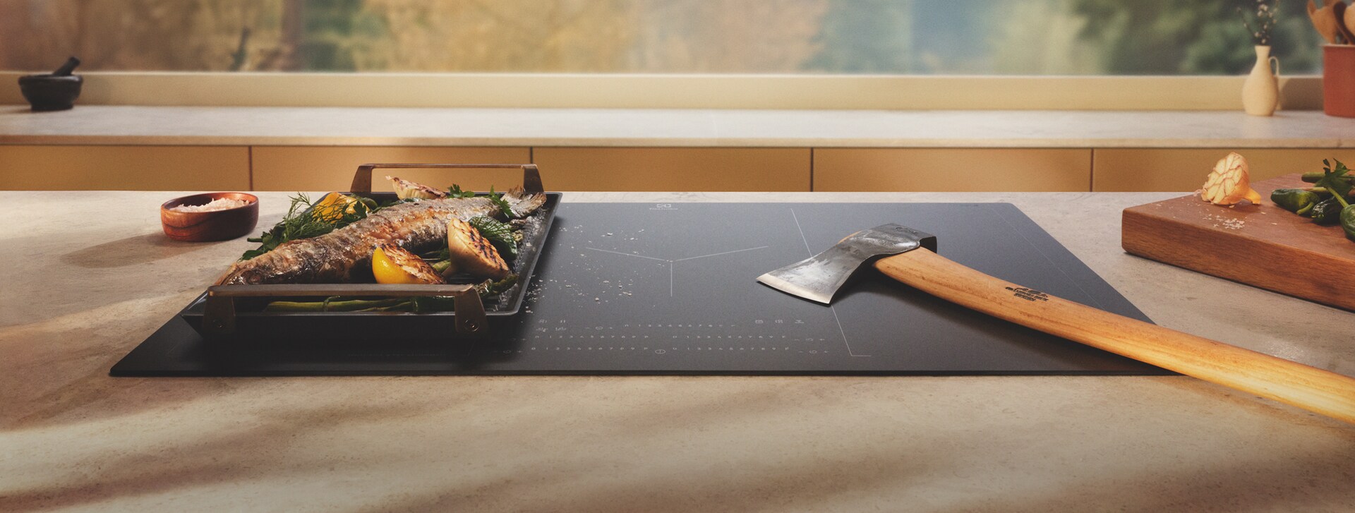 An axe is placed on an induction hob with SaphirMatt surface next to grilled food.